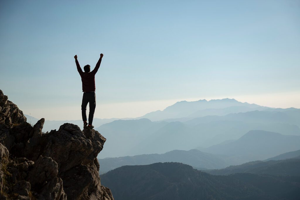 A man standing triumphantly at the top of a mountain peak.
